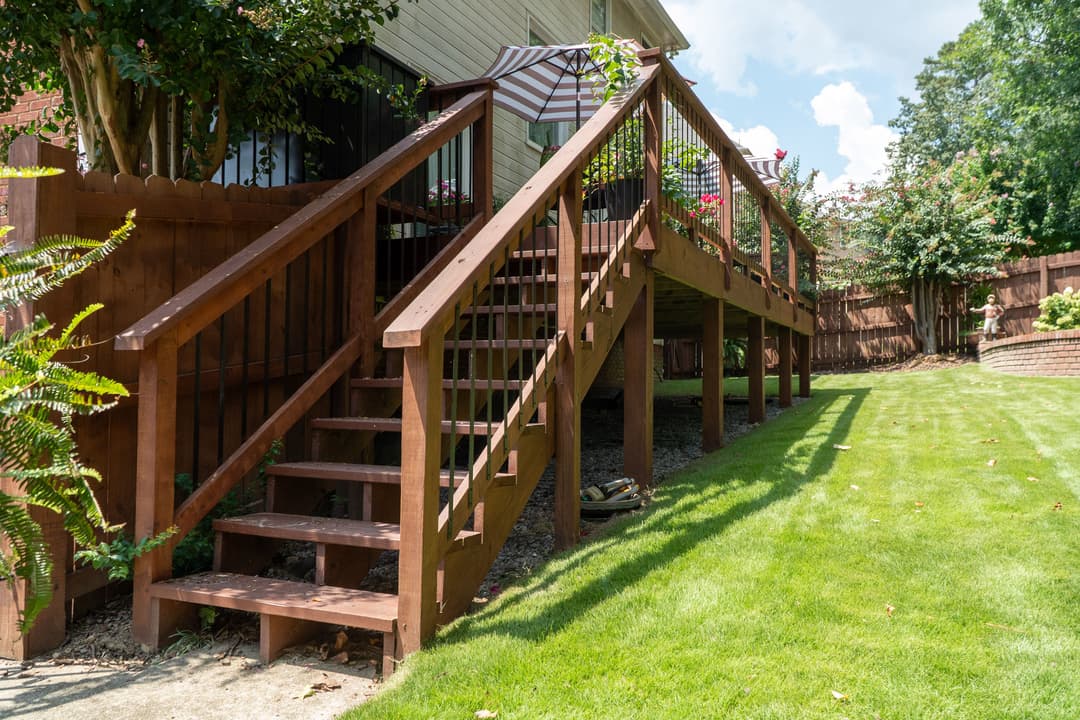 Wooden deck with steps leading to backyard, surrounded by greenery and flowers.