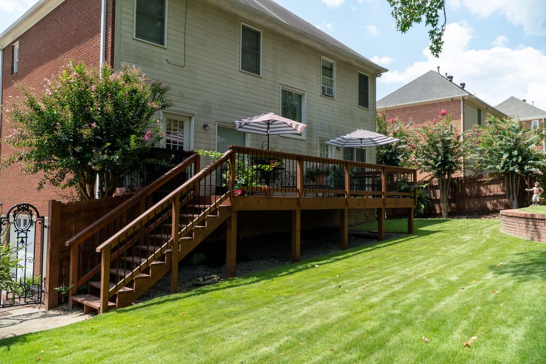 Spacious backyard deck with umbrellas, lush green lawn, and charming landscaping.