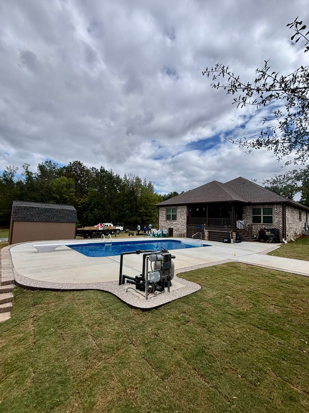 Backyard view of a house with a pool, shed, and cloudy sky, ideal for outdoor relaxation.