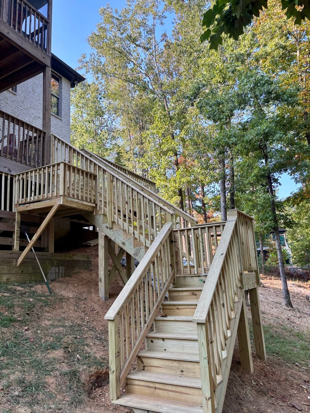 Wooden outdoor stairs leading to a house, surrounded by trees and a clear blue sky.