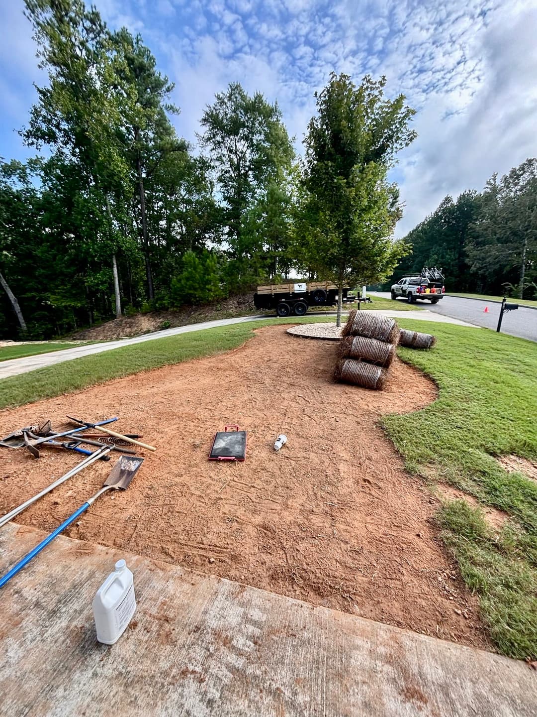 Landscaping project with straw bales, tools, and fresh soil near a residential area.