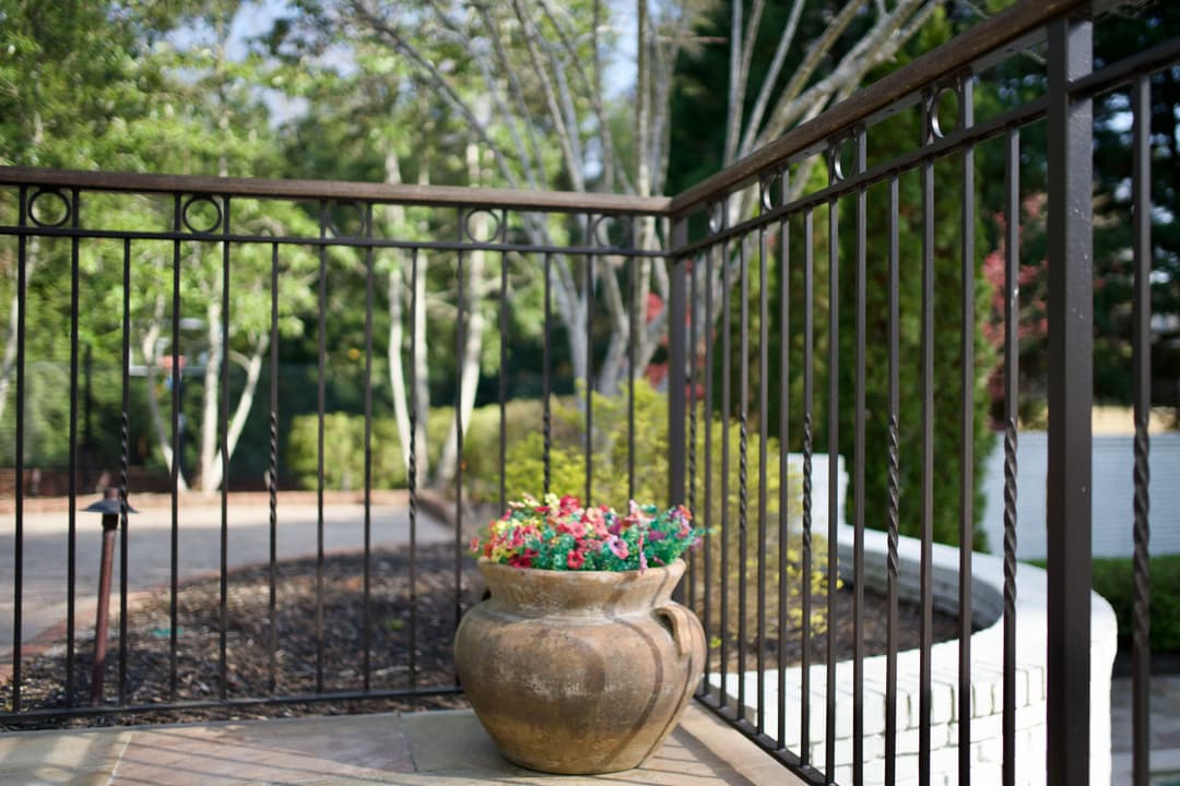 Clay pot with colorful flowers on a patio surrounded by greenery and railing.