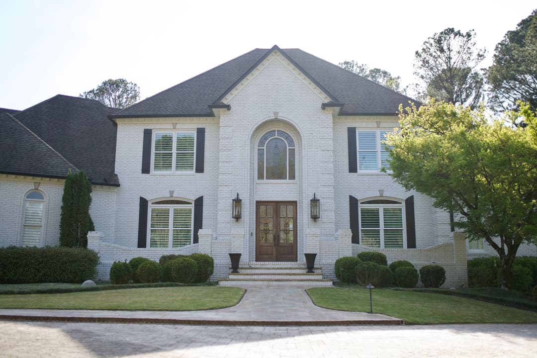 Elegant white brick house with large front windows, wooden double doors, and landscaped yard.