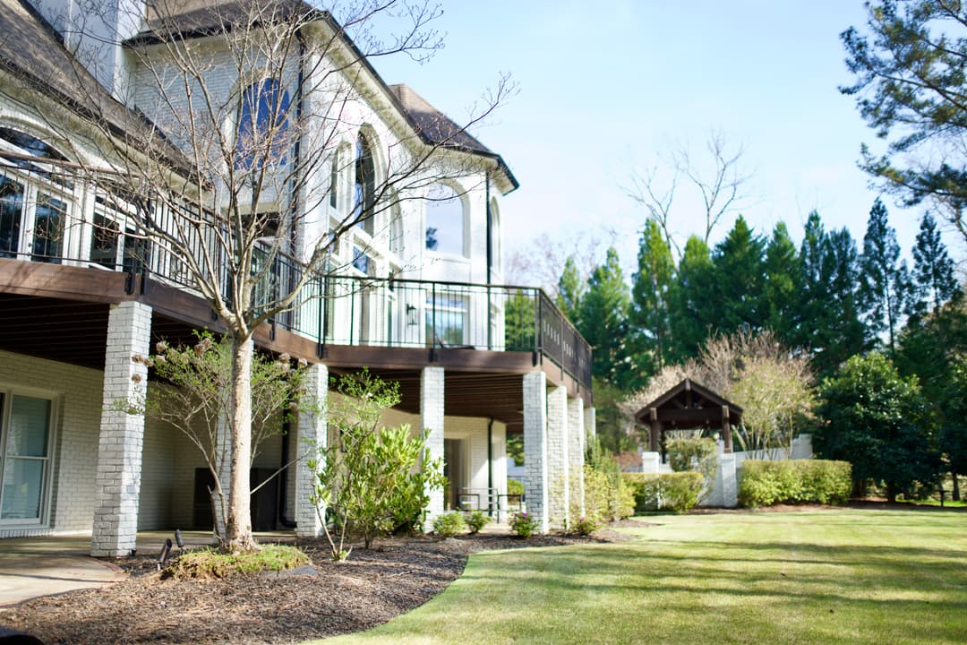Elegant two-story home with a spacious deck overlooking a manicured lawn and garden.