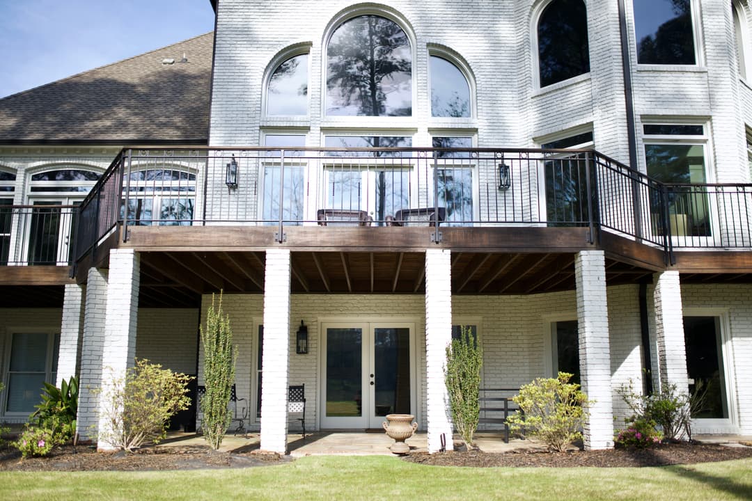 Modern two-story house with a spacious balcony and large windows, surrounded by manicured landscaping.