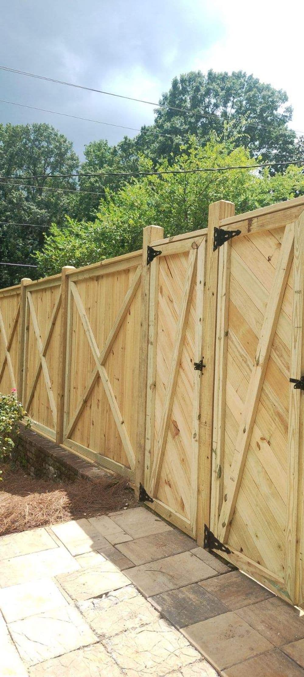 Wooden privacy fence with diagonal patterns, surrounded by greenery and a stone path.
