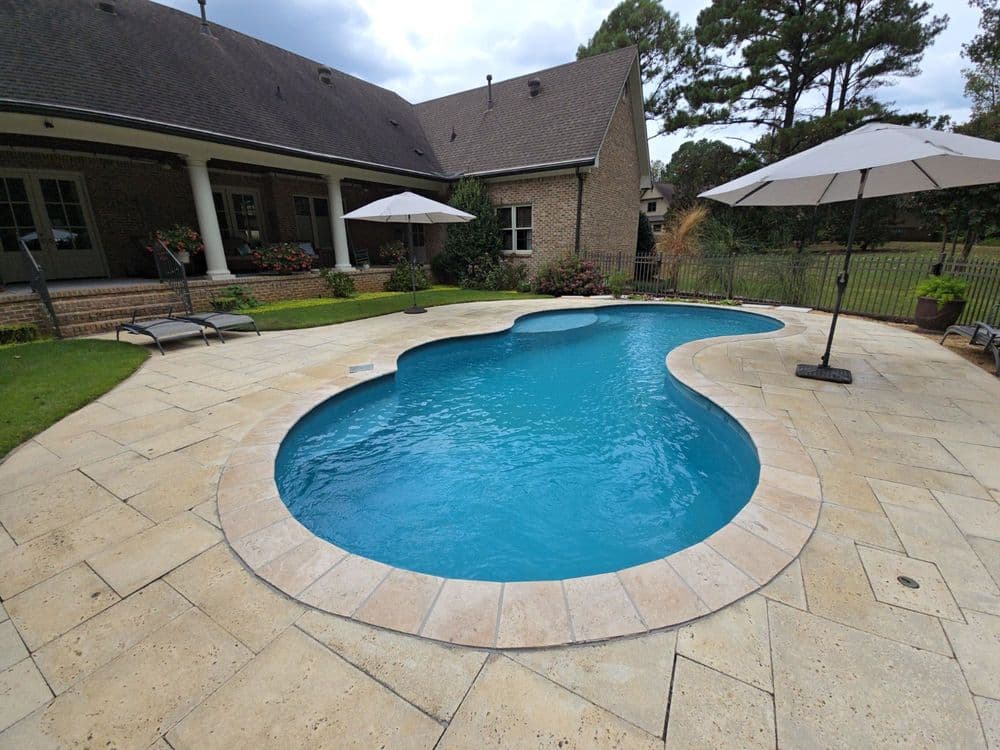 Backyard with a kidney-shaped swimming pool, lounge chairs, and umbrellas on a stone patio.