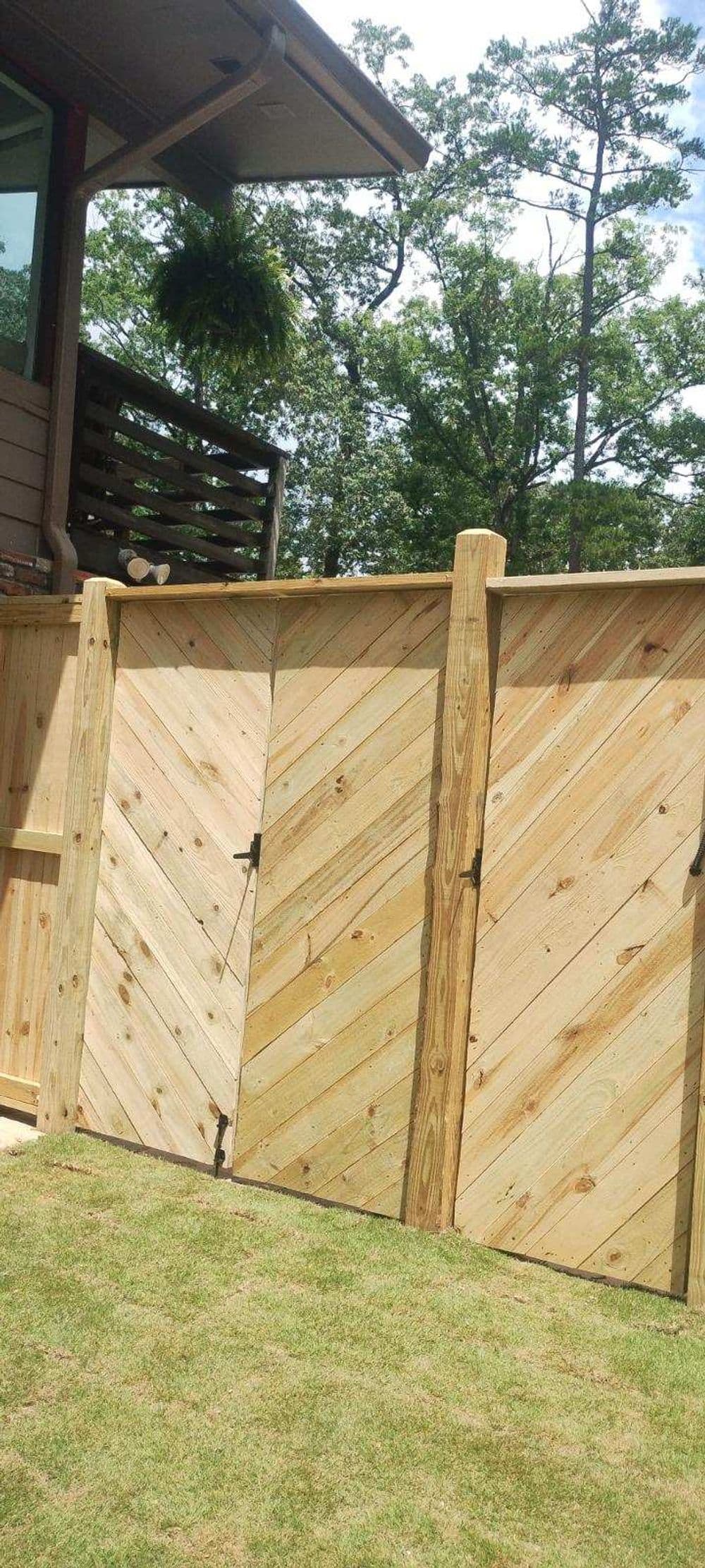 Wooden chevron-patterned gate with hinges, surrounded by greenery and a house.