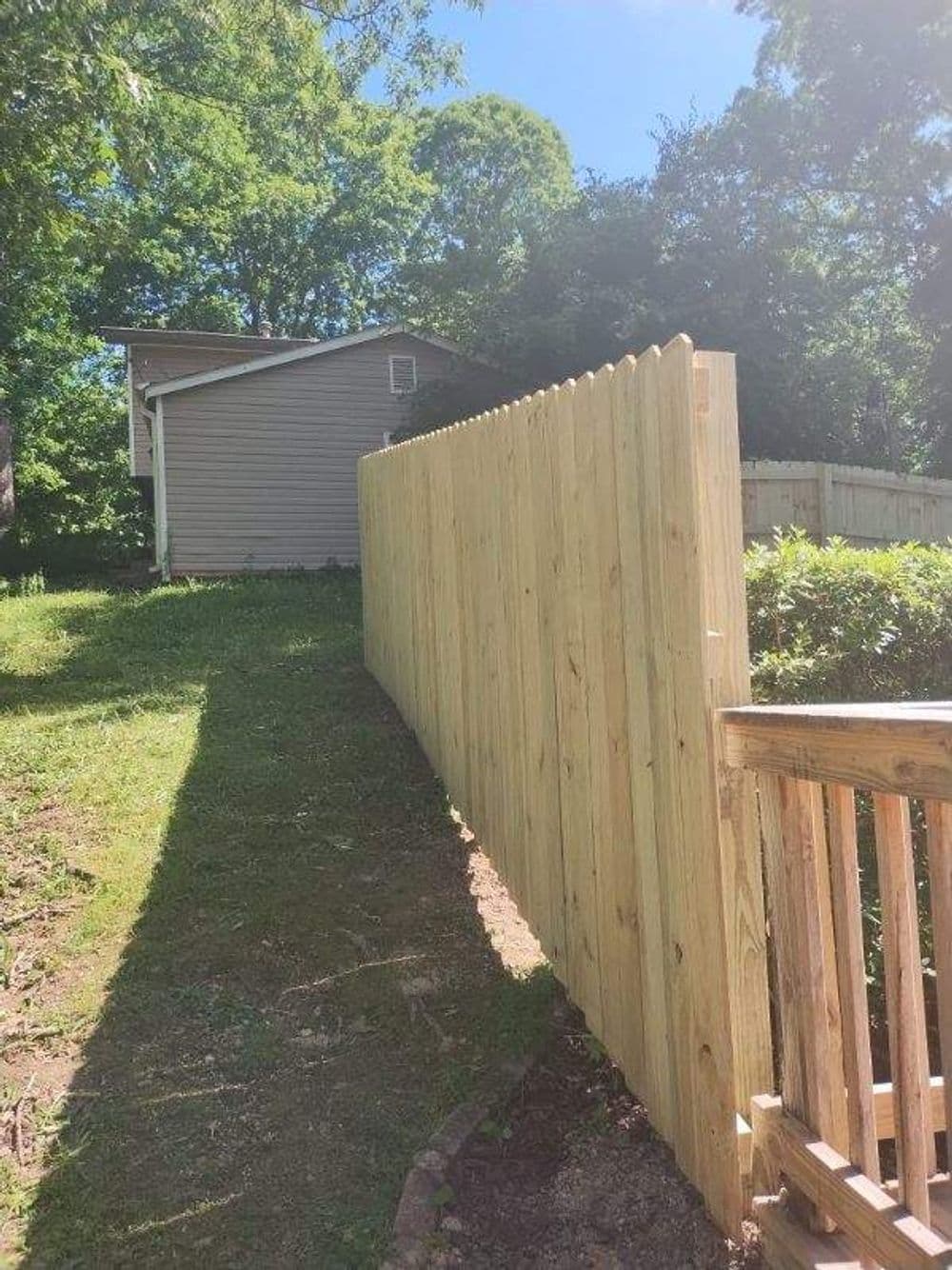 Wooden fence along a grassy path leading to a house under clear blue sky.