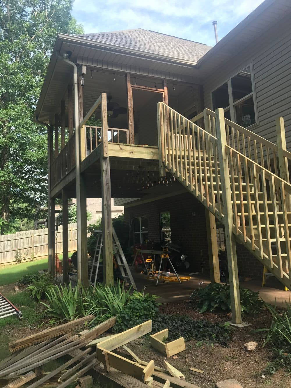 Newly constructed wooden deck with stairs, surrounded by greenery and construction tools.
