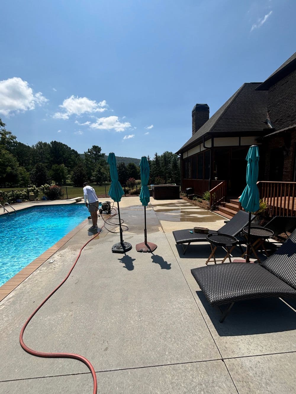 Person cleaning poolside area with umbrellas and lounge chairs under a sunny sky.