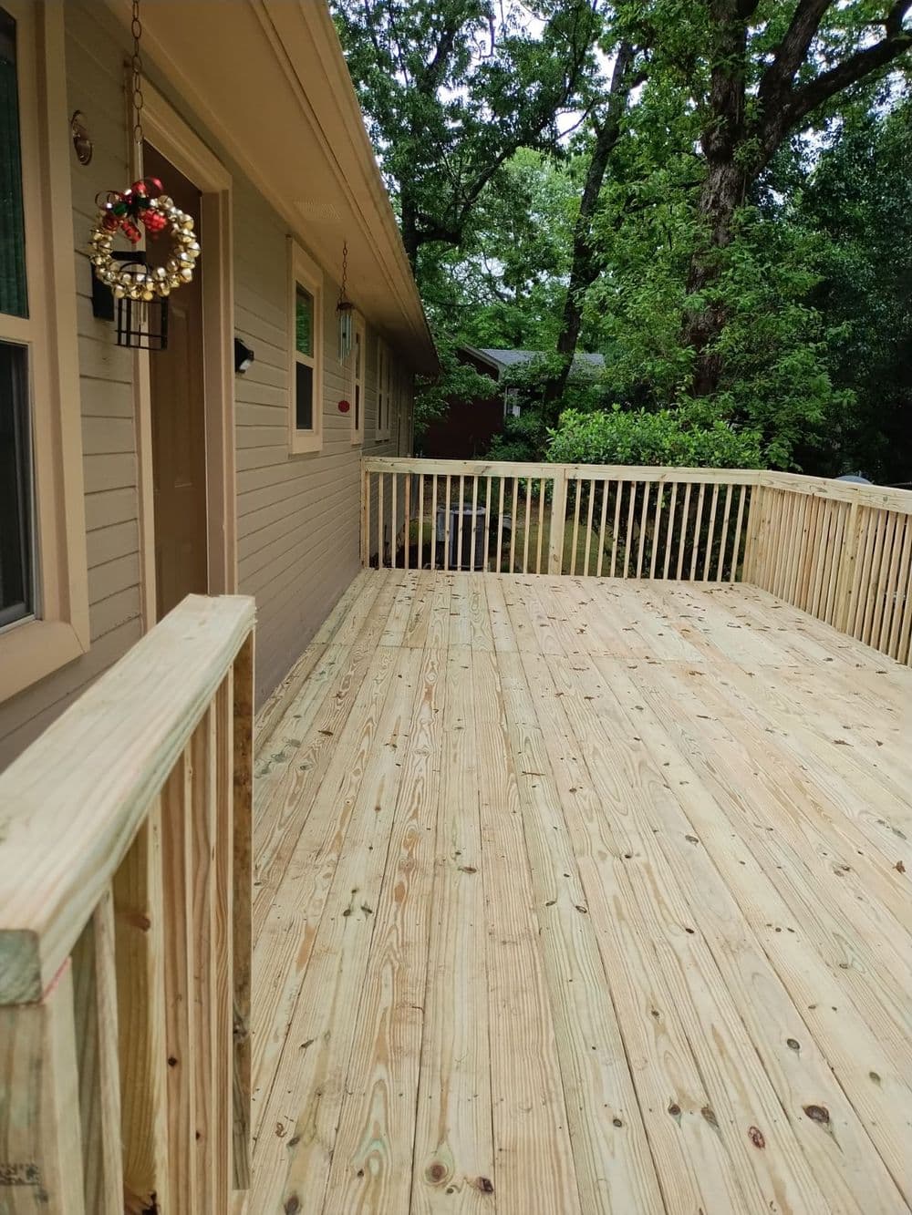 Newly constructed wooden deck with railing outside a house, surrounded by trees.