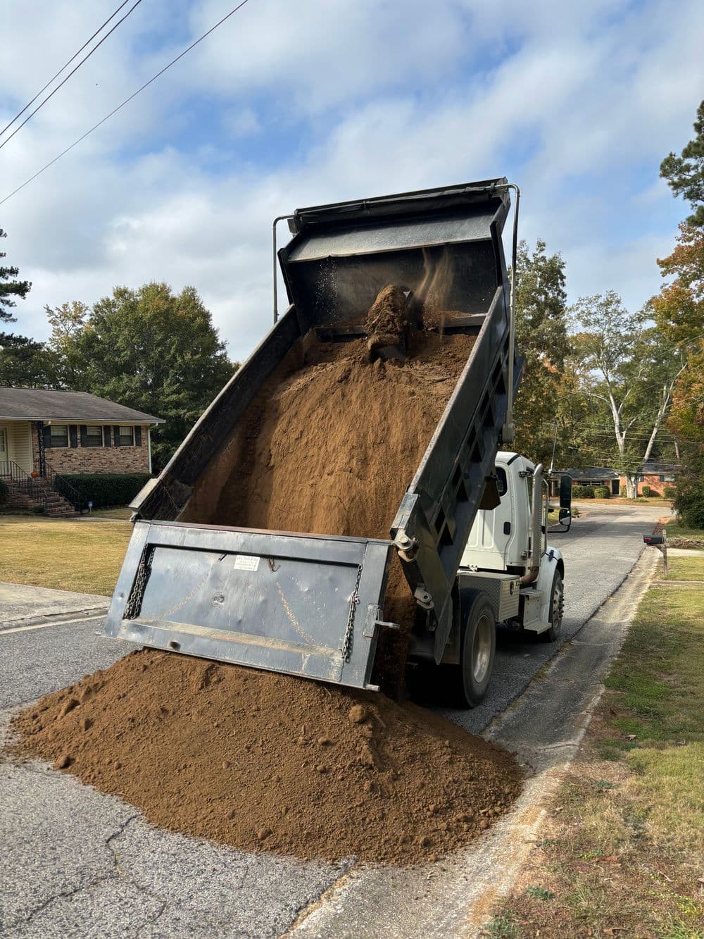 Dump truck unloading soil onto the street in a residential area.
