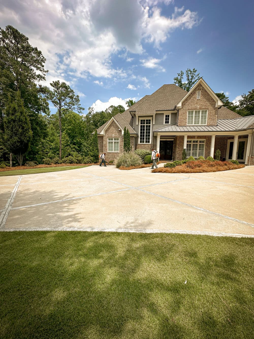 Landscapers maintaining yard near a modern brick house on a sunny day.