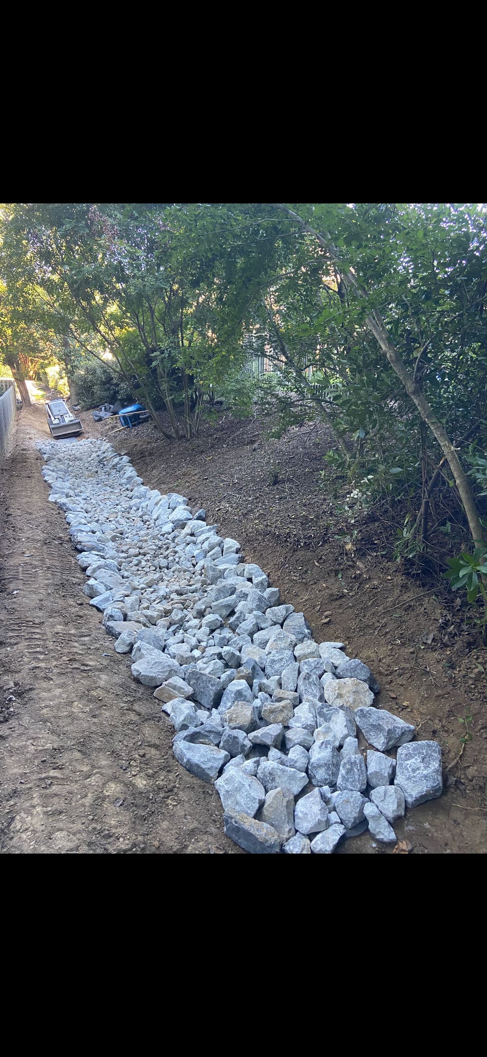 Stone pathway lined with large rocks through a wooded area, showcasing natural landscaping.