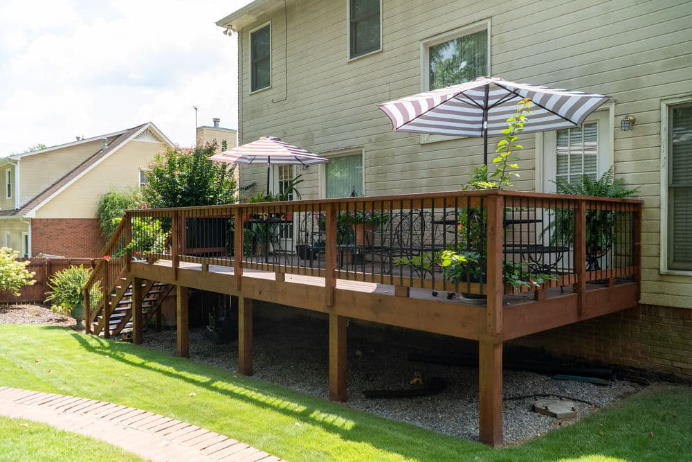 Spacious wooden deck with umbrellas and plants, adjacent to a home's backyard.