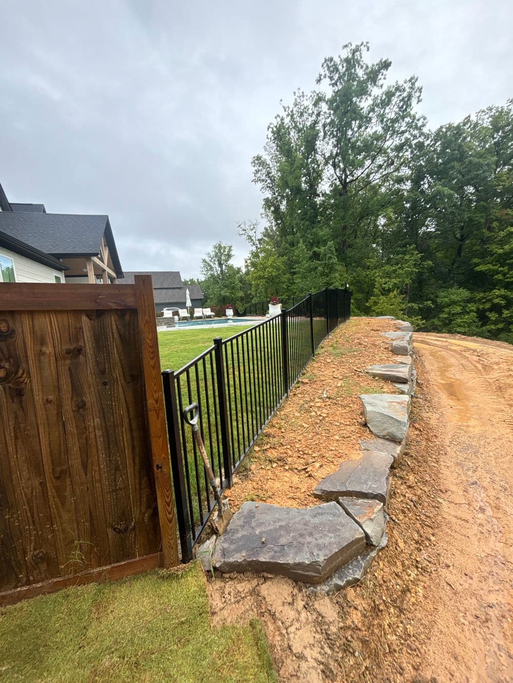 Black metal fence along dirt path with stacked stones beside a grassy area and trees.