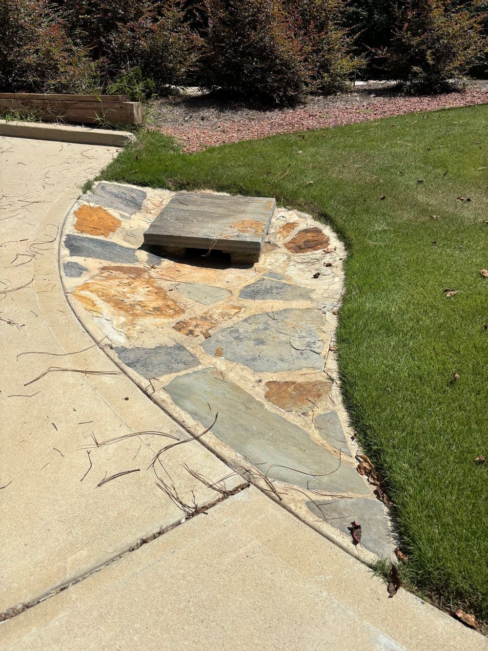 Stone pathway with a wooden platform and surrounding green grass in a landscaped yard.