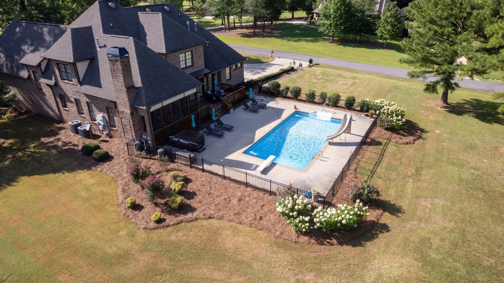 Aerial view of a house with a pool and landscaped backyard in a sunny neighborhood.