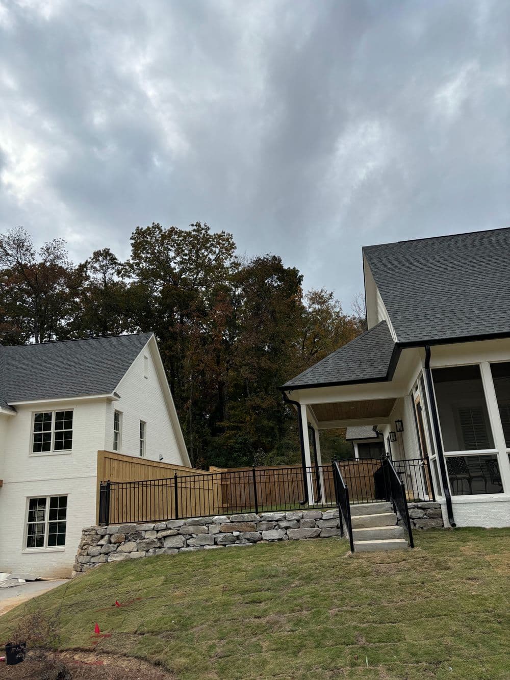 Modern white house with stone landscaping and dark roof, set against a wooded background.