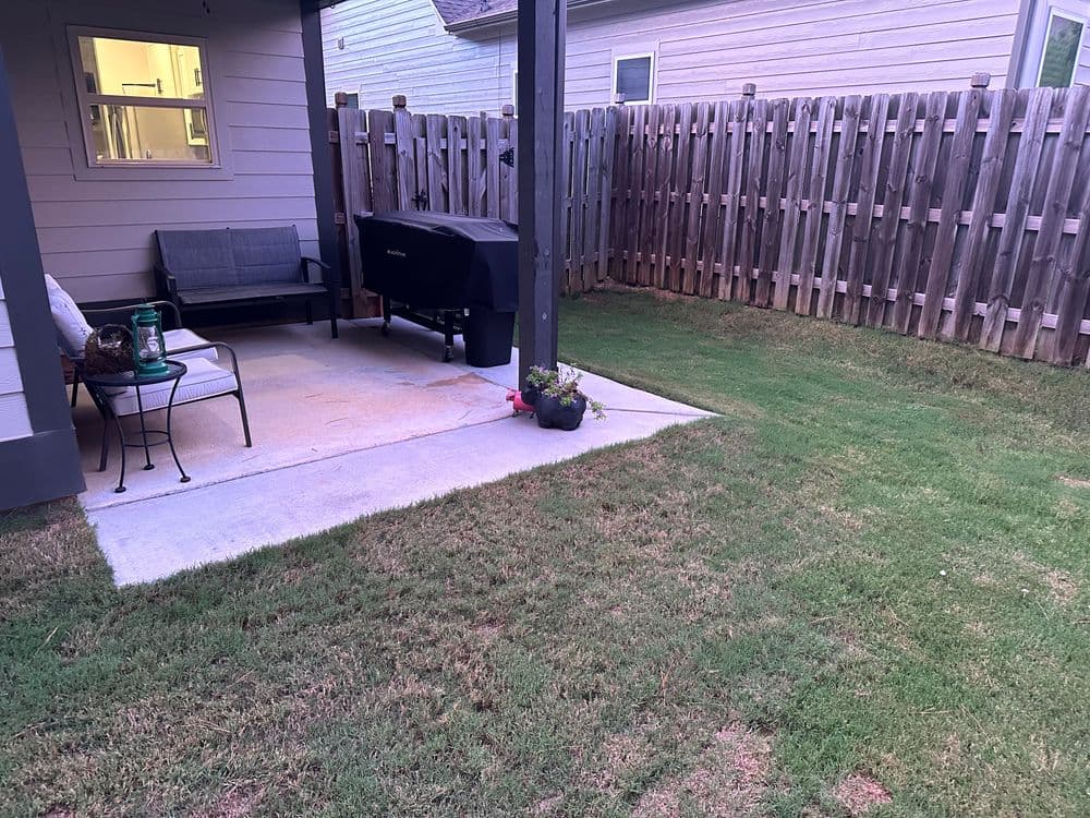 Patio area with seating and grill, surrounded by a grassy lawn and wooden fence.