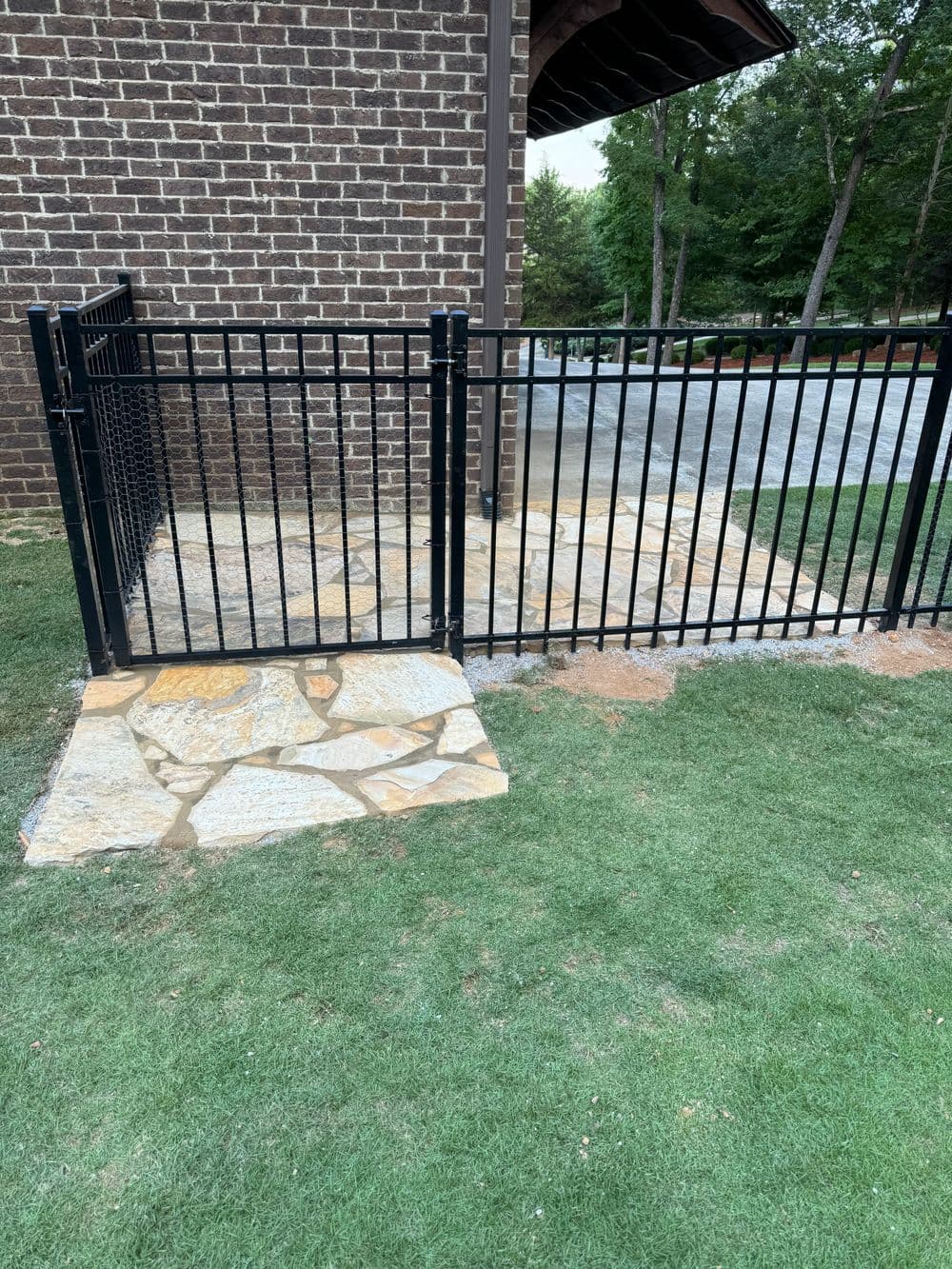Black metal fence enclosing a stone pathway beside a brick building, with green grass nearby.