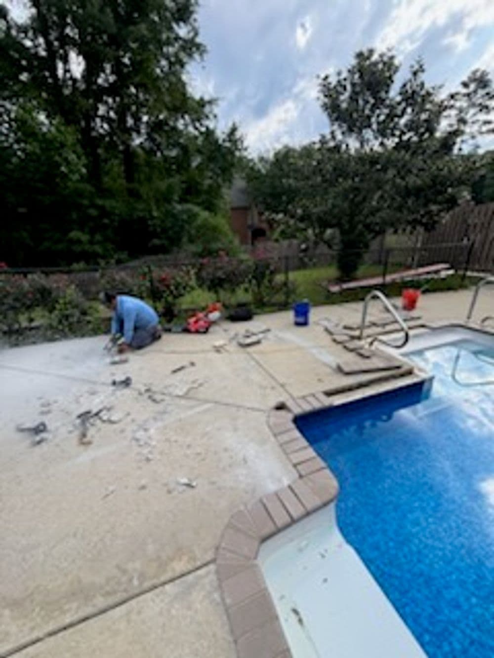 Worker repairing a pool deck beside a blue swimming pool with rehabilitation tools nearby.