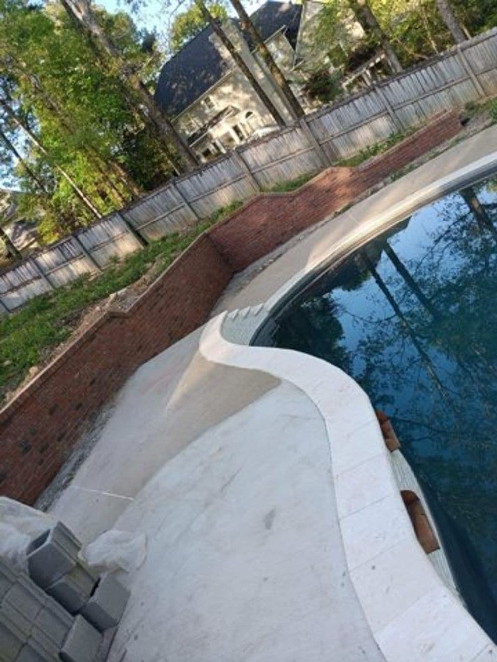 Poolside renovation with curved coping, brick wall, and surrounding landscaping.