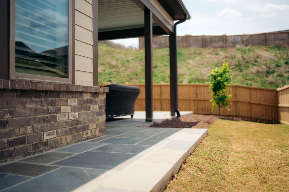 Patio area with stone flooring, brick wall, and fenced backyard featuring a small tree.