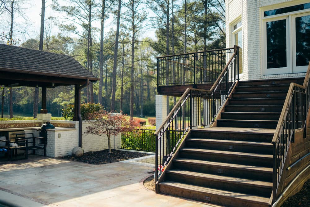 Modern outdoor patio with wooden stairs, railing, and landscaped surroundings.