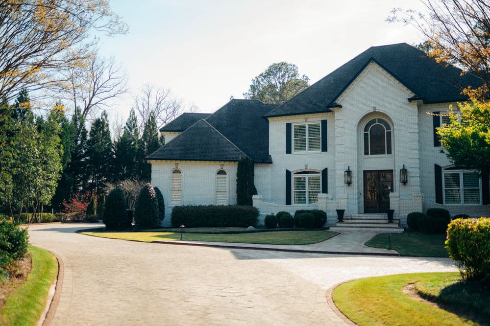 Elegant white luxury home with a curved driveway and manicured landscaping on a sunny day.