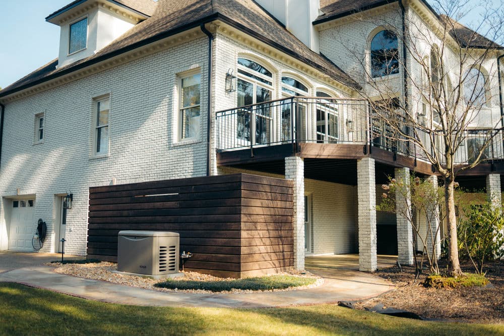 Modern brick house with wooden deck, landscaping, and air conditioning unit outside.