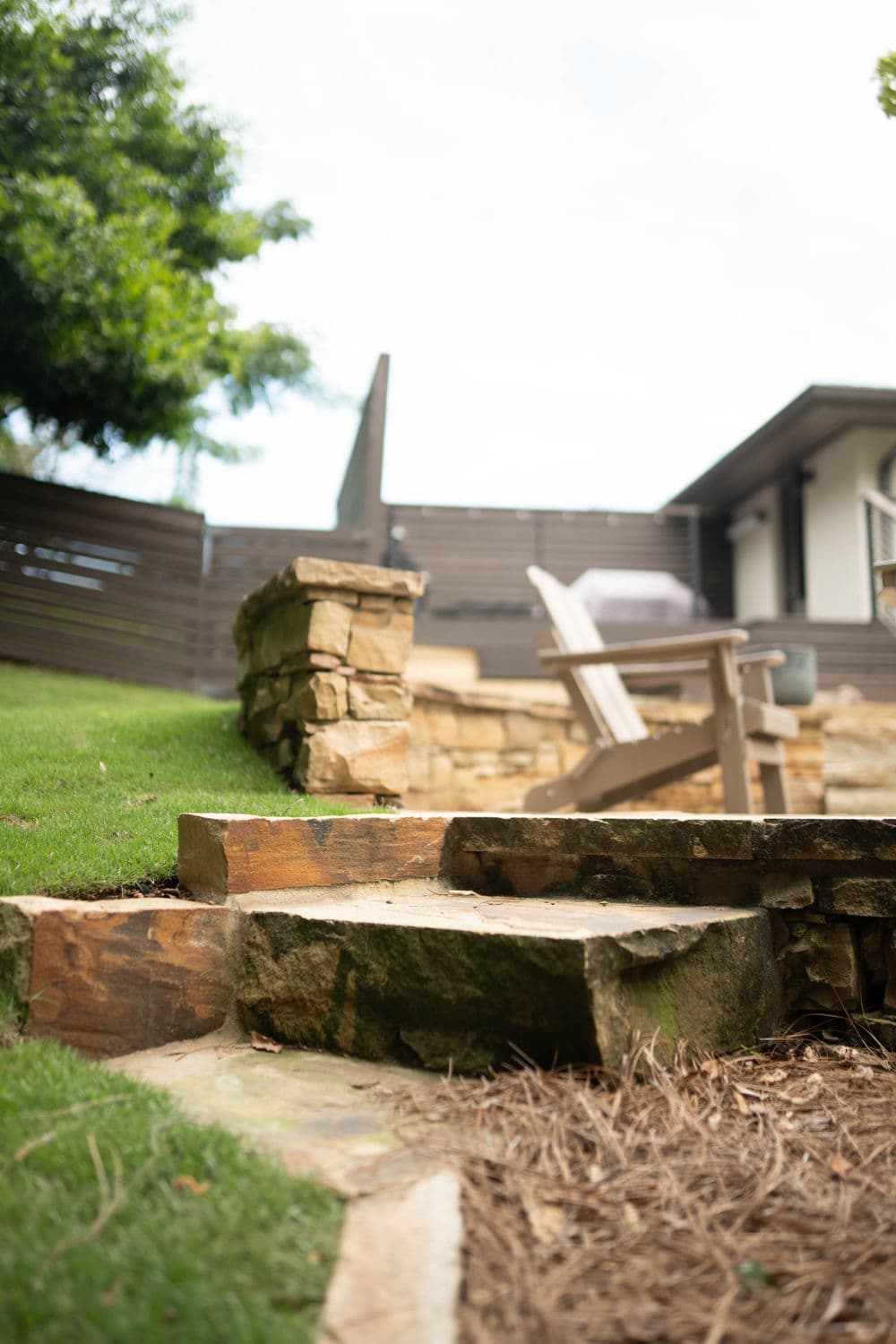 Stone steps lead to a well-maintained garden with wooden seating and a modern home in the background.