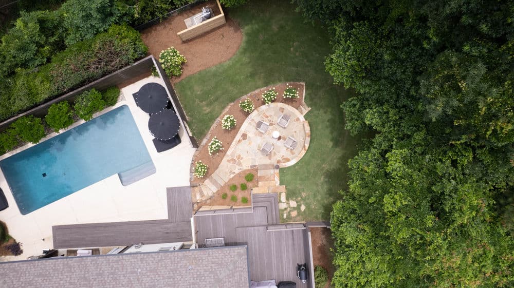Aerial view of a landscaped backyard featuring a pool, patio, and lush greenery.