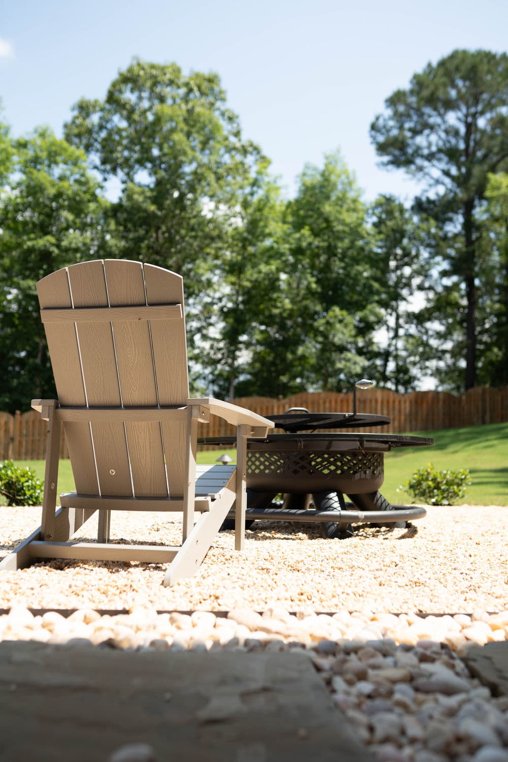 Adirondack chair by fire pit in a serene backyard setting with lush greenery.