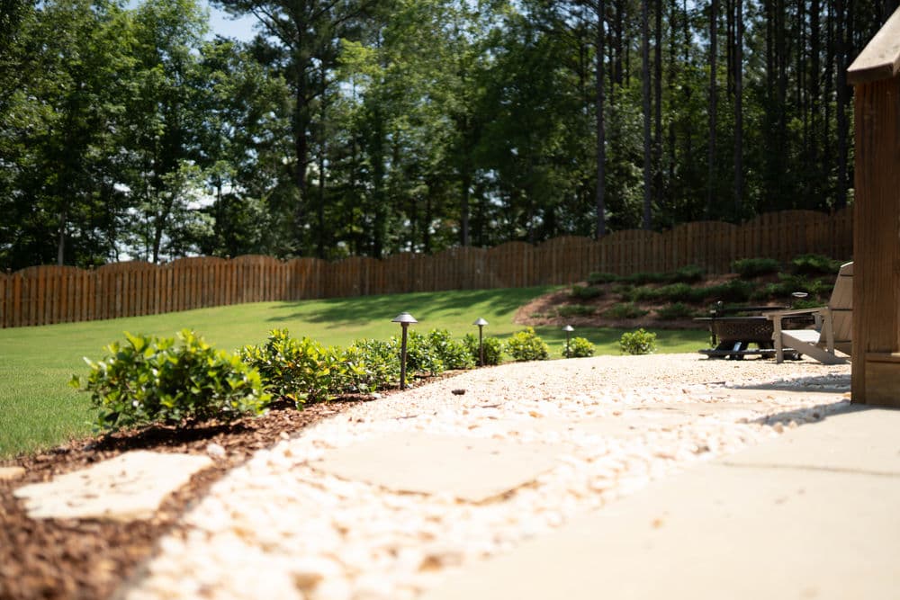 Backyard patio with stone path, landscaping, and wooden fence under clear blue sky.