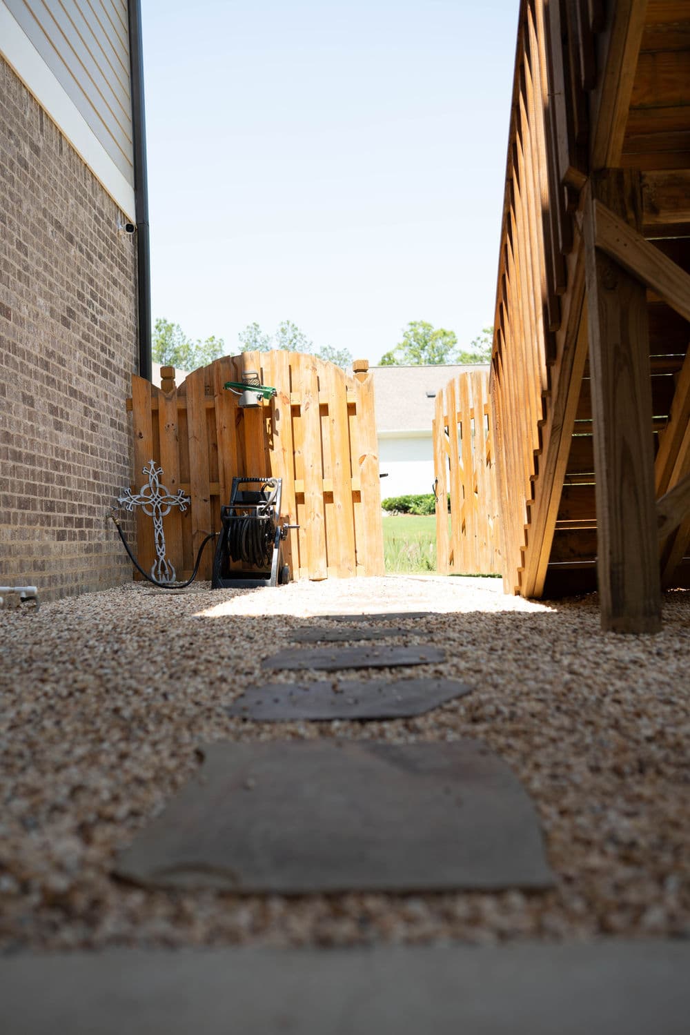 Gravel pathway leading to a wooden fence and stairs beside a brick wall.
